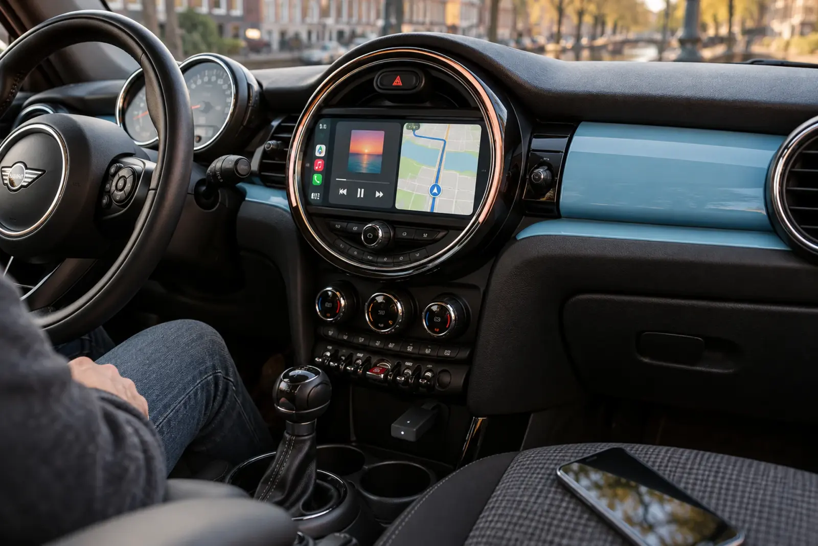 Android Auto met muziek en navigatie op het ronde scherm van een Mini, telefoon op de stoel, onderweg in Heerlen
